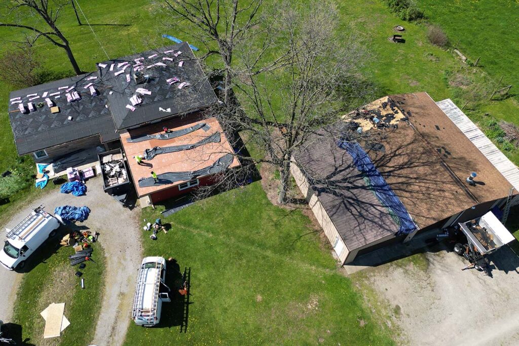 Action shot of the home ready for new shingles. The rubber roof has been removed, and preparations are underway for the new rubber overlay. The detached garage was just beginning to have its shingles removed.