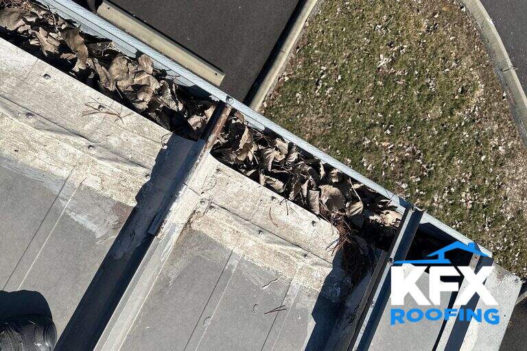 Clogged gutter filled with dead leaves and debris viewed from rooftop during inspection