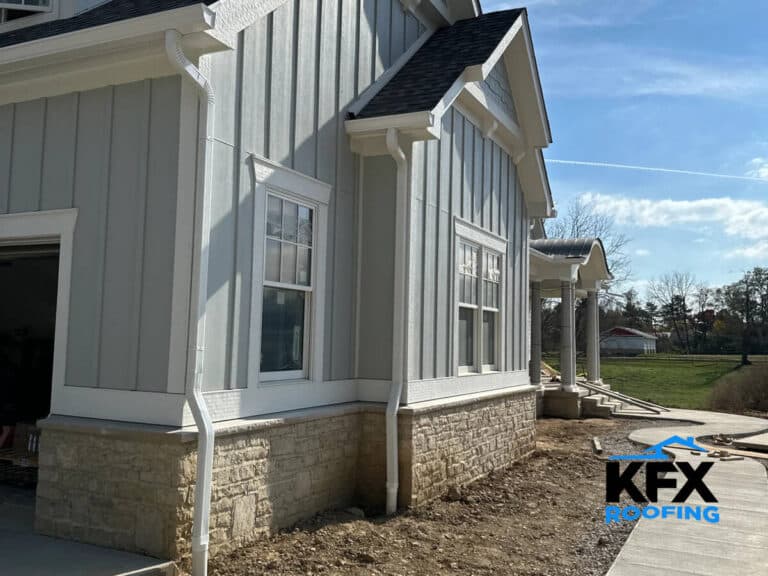 New construction home with white 6-inch gutters and downspouts installed on gray board and batten siding
